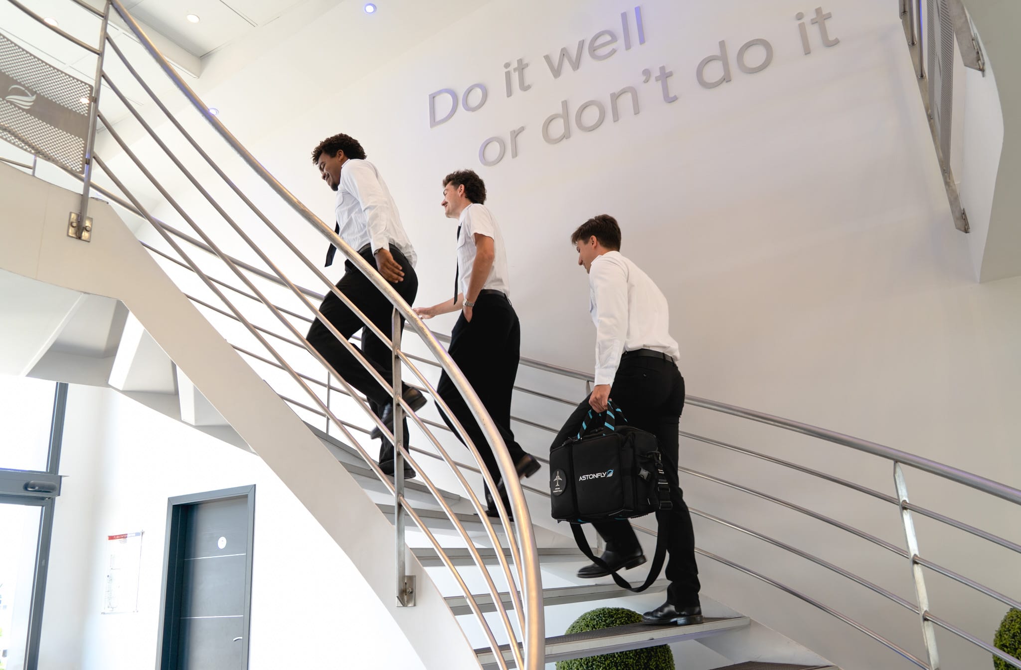 Élèves pilotes Astonfly montant l'escalier sous la devise « Do it well or don't do it »
